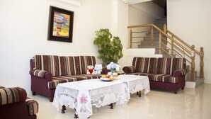 A living room with two sofas, a table with a lace tablecloth, a potted plant, and a staircase in the background. - Na Na Ya Ji Bed and Breakfast (Taitung)