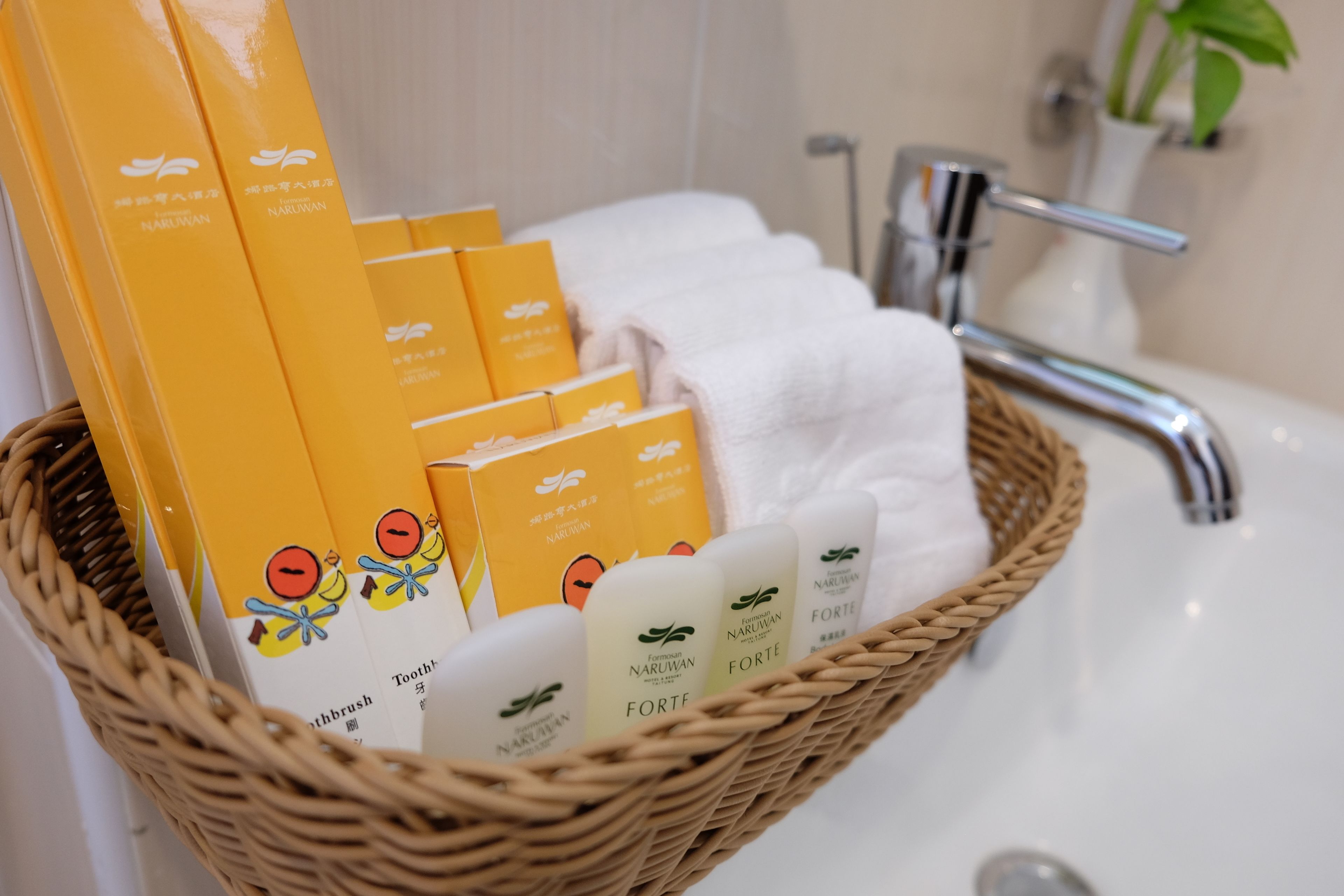 A wicker basket containing toiletries and towels on a bathroom sink.