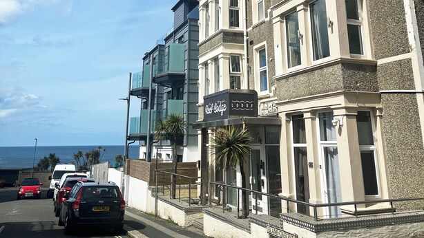 Ein Küstenhotel mit moderner Fassade, einem gut sichtbaren Schild für Reel Lodge und Blick auf das Meer.