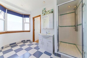 A bathroom with a checkered floor, a sink, cabinets, a mirror, and a shower area.
