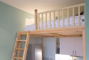 A bunk bed with a wooden ladder, a kitchen area with cabinets and a refrigerator, and a window with daylight.