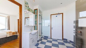 Ein modernes Schlafzimmer mit Schachbrettfußboden, einem Bett, einem Badezimmer mit Dusche und einer weißen Tür.