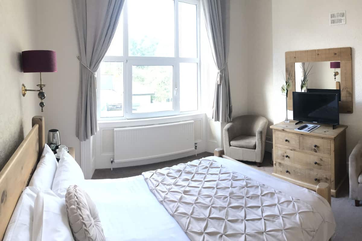 A hotel room with a bed, two armchairs, a dresser, a television, and a window with curtains.