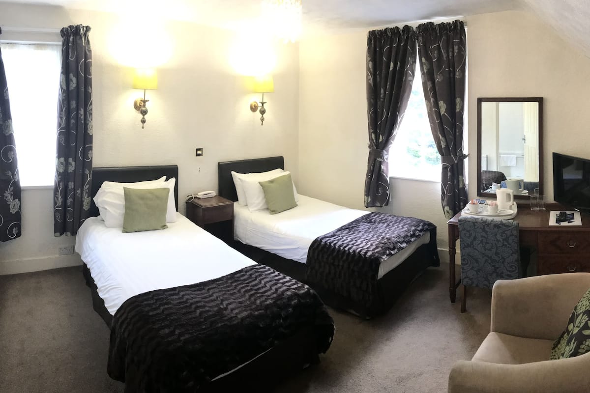 A hotel room with two beds, a desk with a chair, a television, and a mirror.