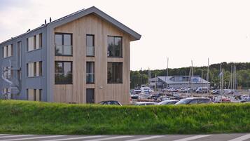 A modern building with a wooden facade and large windows, adjacent to a marina with boats and cars.
