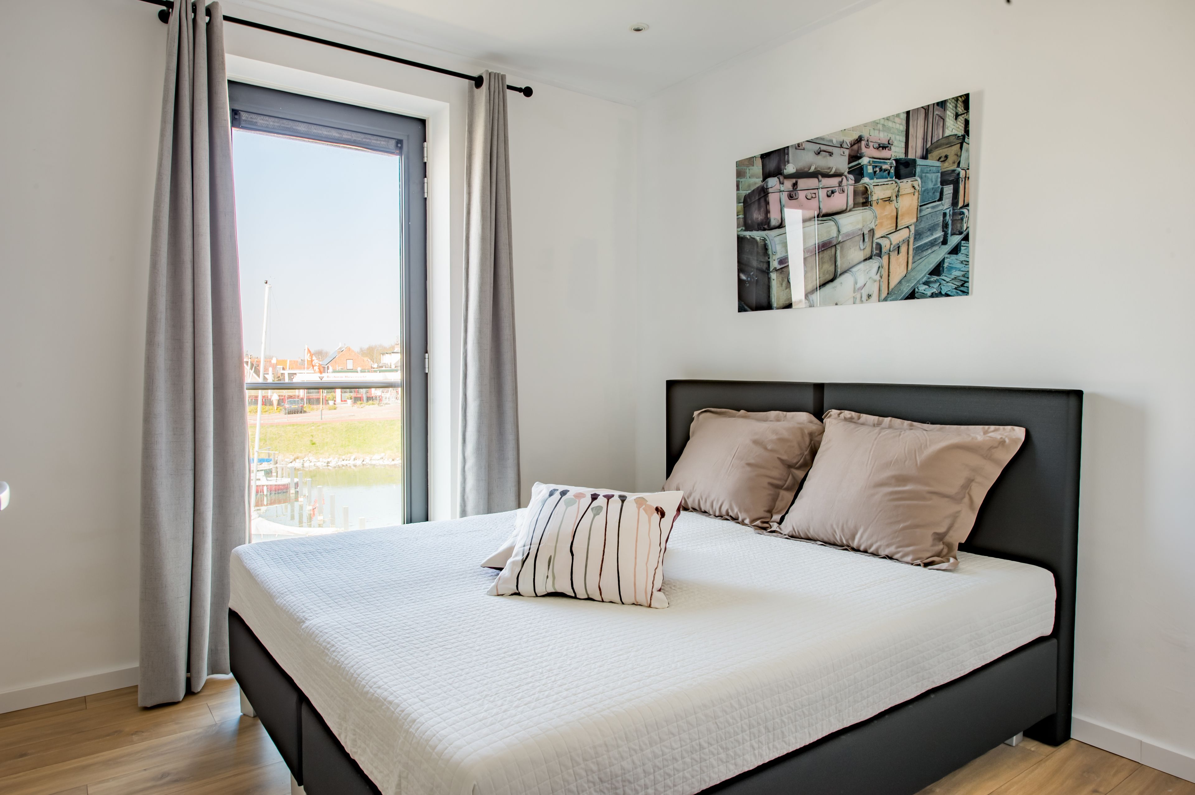 A bedroom with a large bed, a window with curtains, and a painting on the wall.