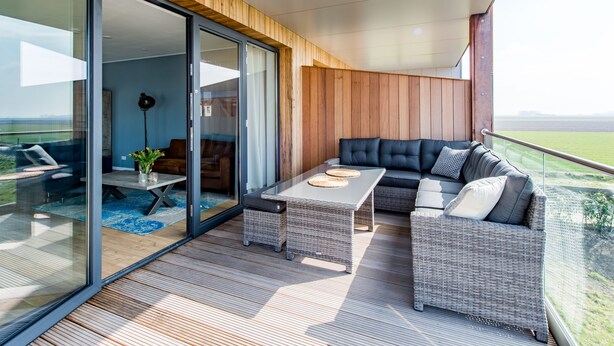 Un espacio exterior moderno con puerta corredera de vidrio, terraza de madera, sofá, mesa de centro y vistas al paisaje.
