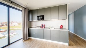 Una cocina moderna con armarios grises, encimera de acero inoxidable y vista a un cuerpo de agua a través de grandes ventanales.