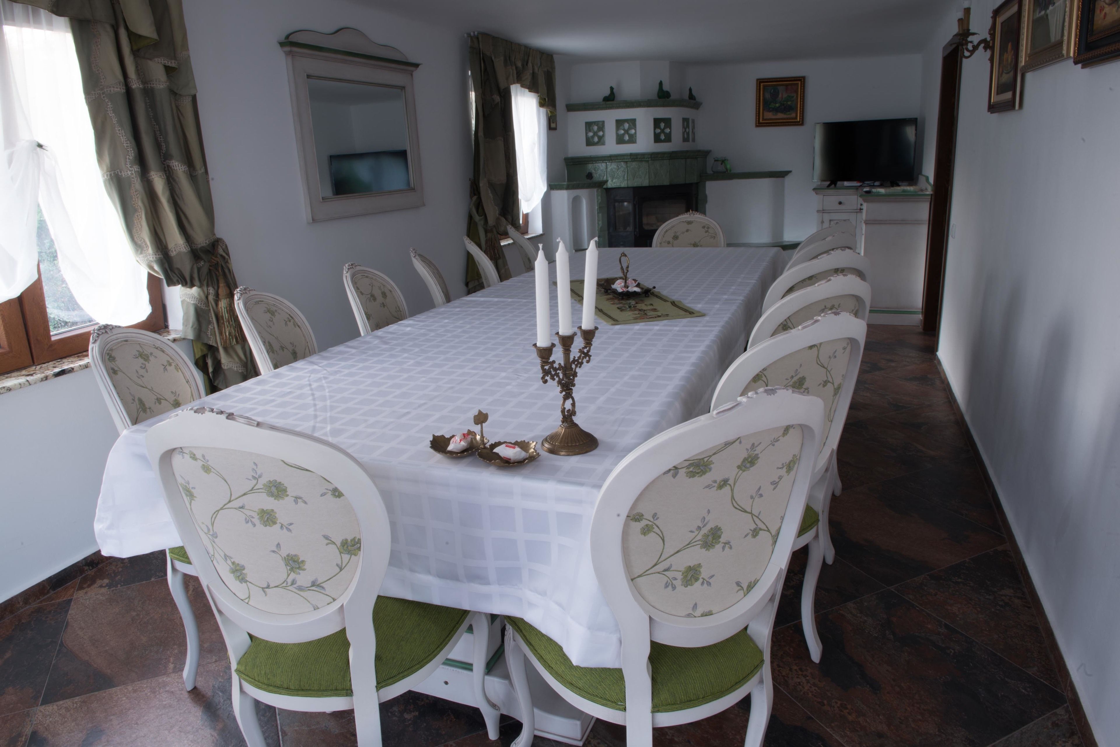 Een eetkamer met een lange tafel, witte stoelen met groene kussens en een witte tafelkleed.