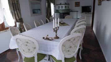 Een eetkamer met een lange tafel, witte stoelen met groene kussens en een witte tafelkleed.