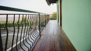 Un balcón de madera con barandilla metálica que da a un jardín y un paisaje distante.