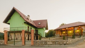 Una casa verde con techo rojo, pared de piedra y un área cercada con escaleras.