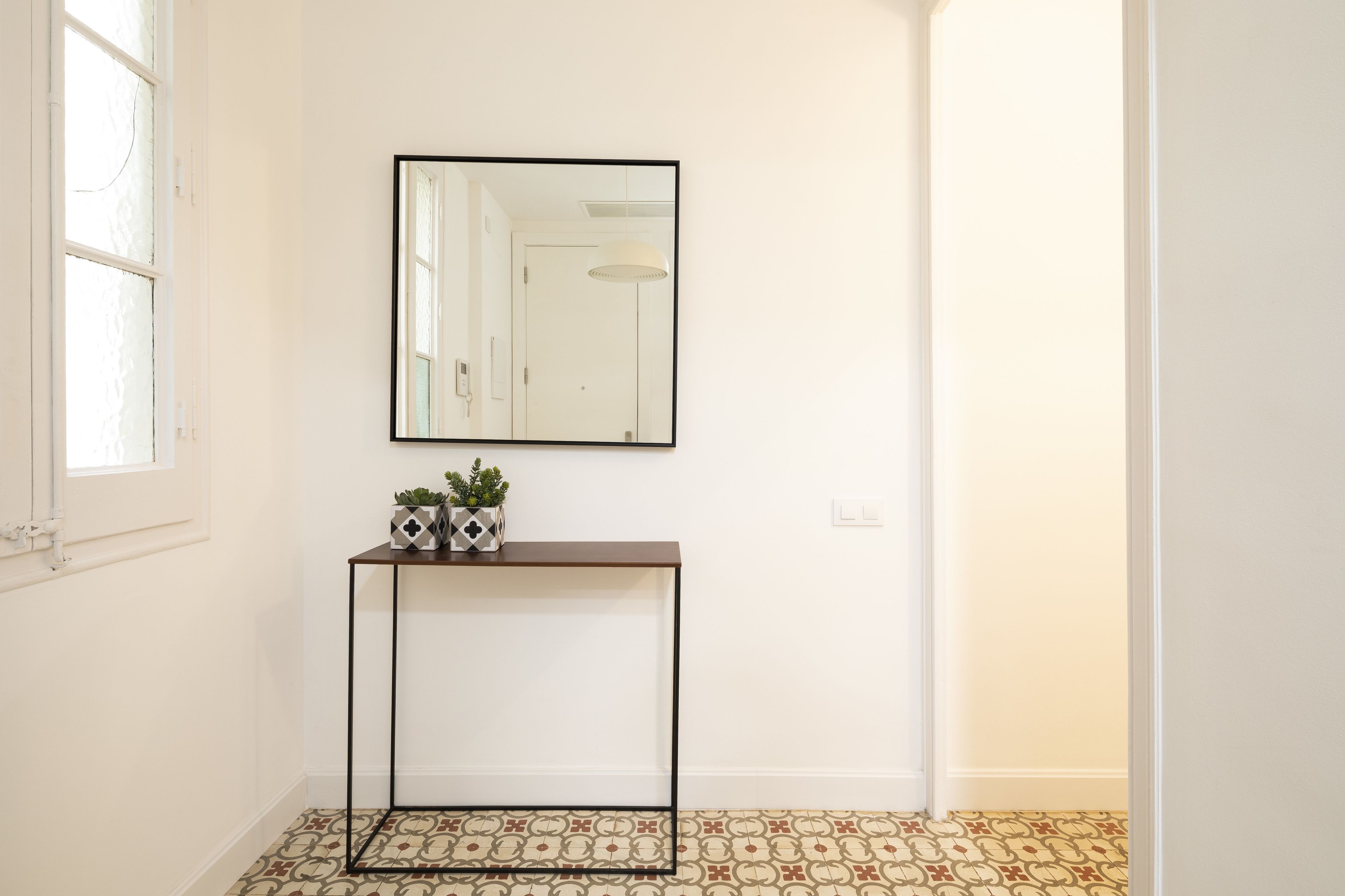 A hallway with patterned flooring, a console table with decorative items, a mirror, and a door.
