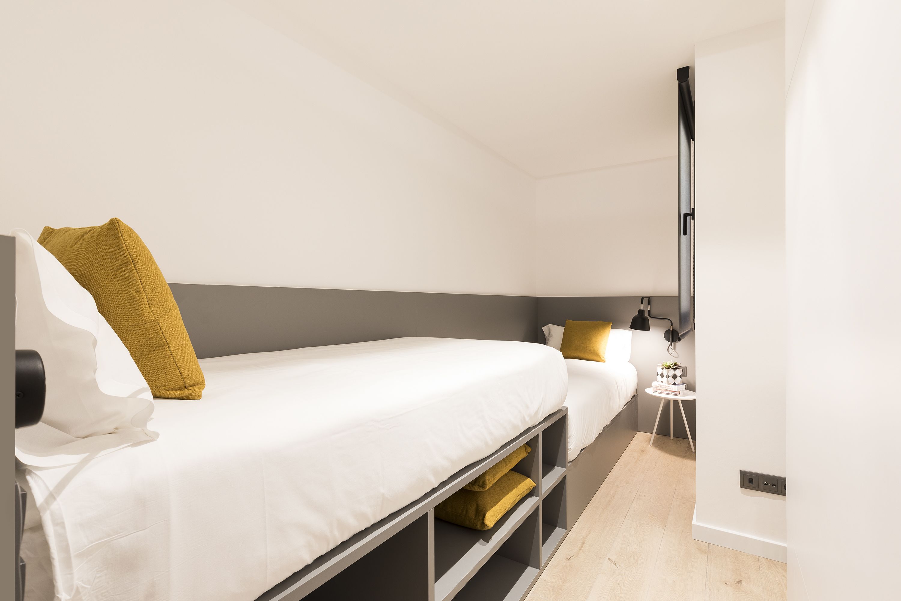 Une chambre d’hôtel moderne avec un lit simple, une petite table de chevet, un téléviseur fixé au mur et un plancher en bois de couleur claire.