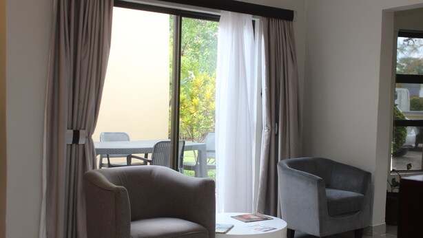 A room with two armchairs, a small white table, and a view of an outdoor area with a table and chairs.