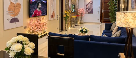 Una sala de estar moderna con un sofá azul, televisor, obras de arte y chimenea.