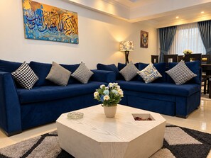 Un salon moderne avec un canapé bleu, une table basse en bois ornée d’un vase de fleurs et un tableau accroché au mur.