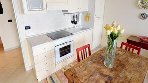 Una cocina compacta con armarios blancos, horno integrado y una mesa de comedor de madera con un florero de flores amarillas.