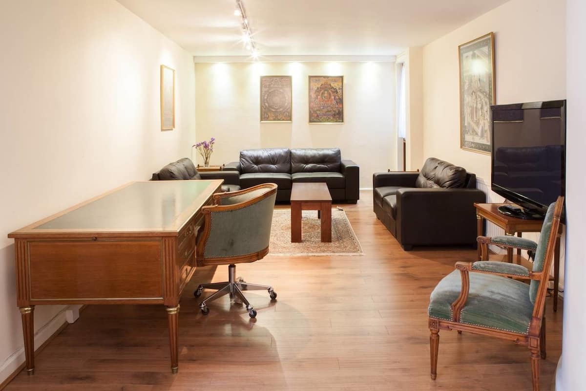 Ein Wohnzimmer mit Couchtisch aus Holz, einem Schreibtisch, zwei Sofas, einem Fernseher und Kunstwerken an den Wänden.