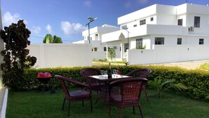 Eine Terrasse mit Korbstühlen und einem Tisch, ein Grill und ein weißes Gebäude im Hintergrund.