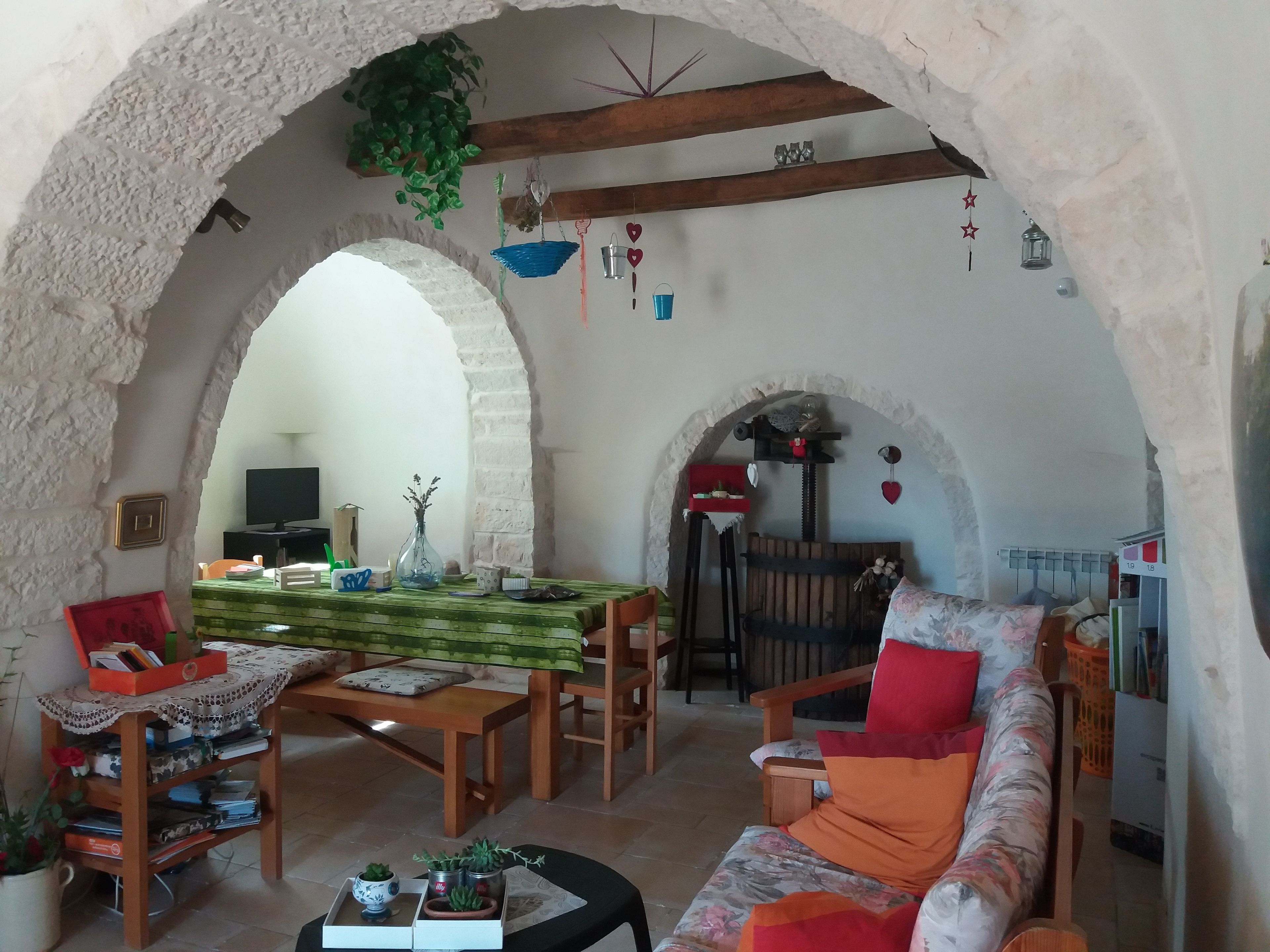Un salon chaleureux avec une table en bois, un canapé et des fauteuils, un plafond en arc de cercle et un téléviseur en arrière-plan.