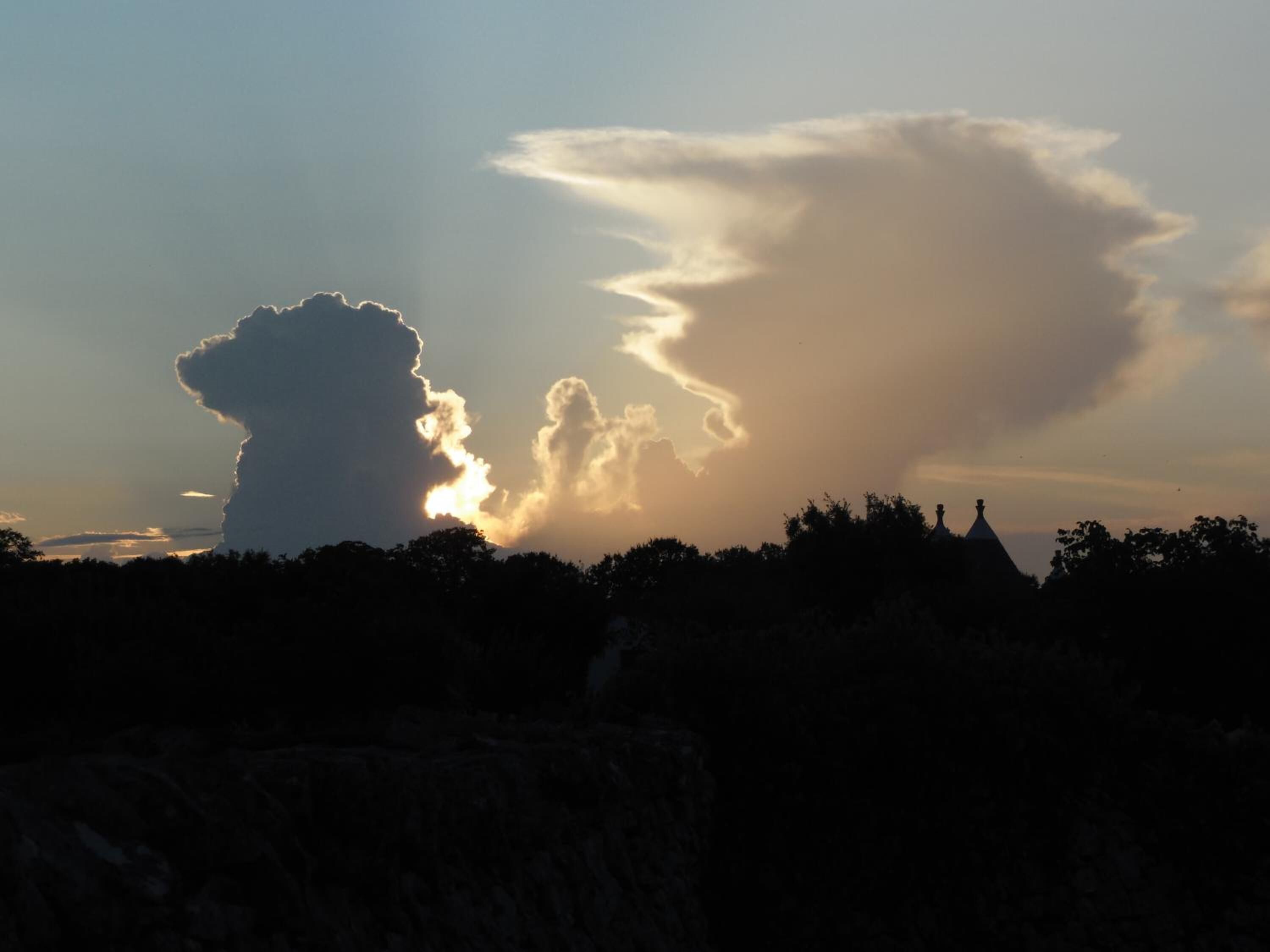 A silhouette of a building with a prominent dome and a large cloud formation in the sky.