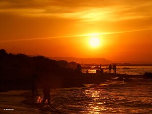 A sunset over a beach with people standing and walking in the water. - Trulli sotto La Cupa (Martina Franca)