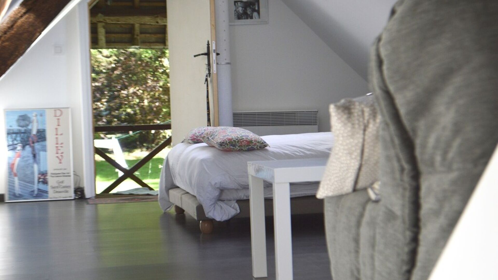 A bedroom with a bed, a nightstand, a window with a view of greenery, and a poster on the wall.