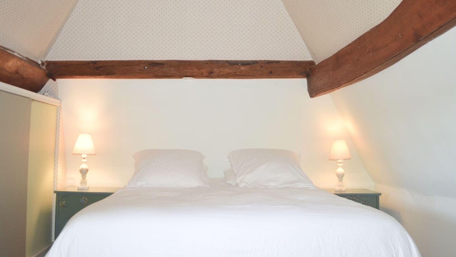 Una camera da letto con un letto singolo, due comodini con lampade e una trave in legno al soffitto.