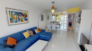 A modern living room with a blue sofa, a white coffee table, and a dining area with a white table and chairs. - Stunning 3BR Apartment with Sea View, Terrace, and Garage in Menton (Menton)