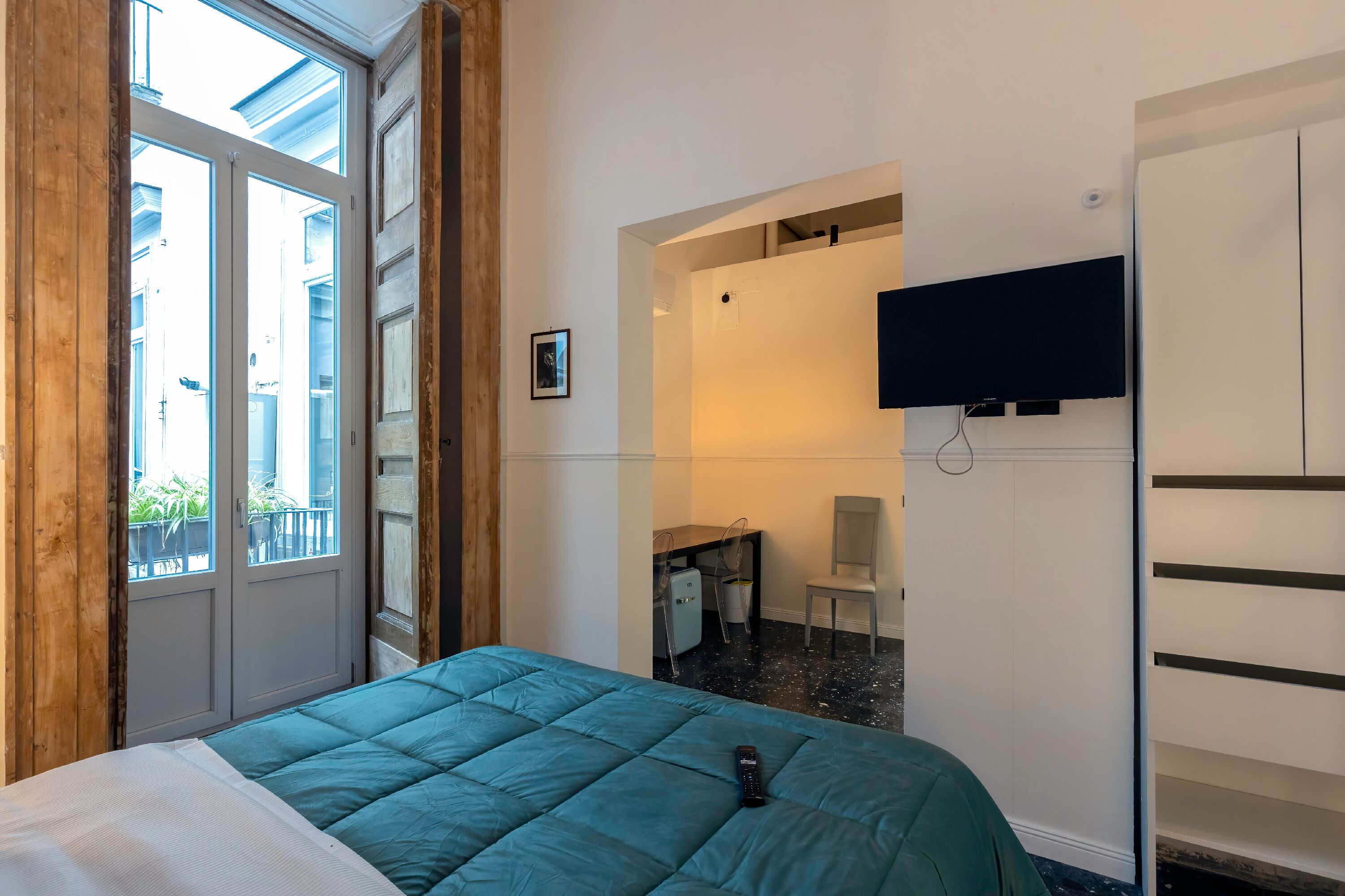 Une chambre d’hôtel comprenant un lit, un téléviseur fixé au mur, un bureau avec une chaise et une armoire.