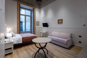 Un dormitorio con cama, mesita de noche con lámpara, mesa redonda, sofá y televisor en la pared.