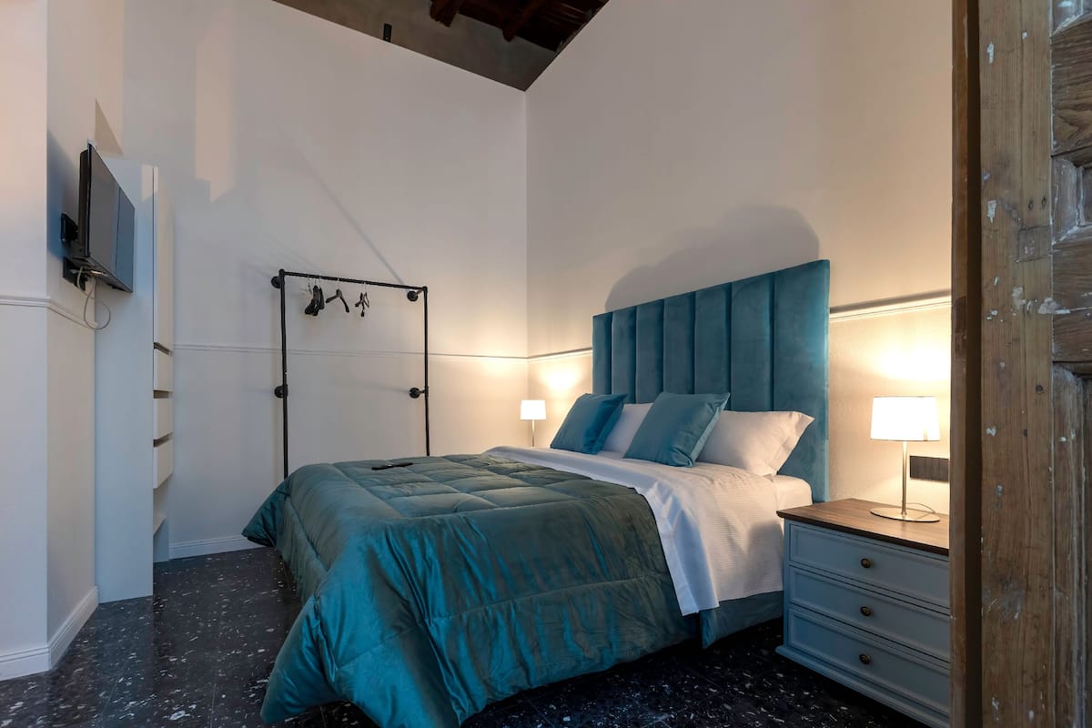 A bedroom with a bed, bedside tables, a TV, and a coat rack.