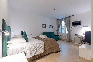 Een hotelkamer met een bed, bureau, stoel, televisie en een raam met gordijnen.