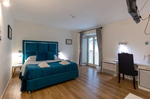 Una camera da letto con un letto color petrolio, pavimento in legno, una scrivania con sedia e una finestra con tende.
