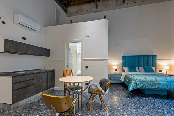 A modern room with a bed, a dining table with chairs, a small kitchen area, and a bathroom.