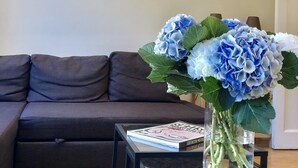 Un salon avec un canapé marron foncé, une table basse en verre sur laquelle repose un livre, et un vase contenant des fleurs bleues.