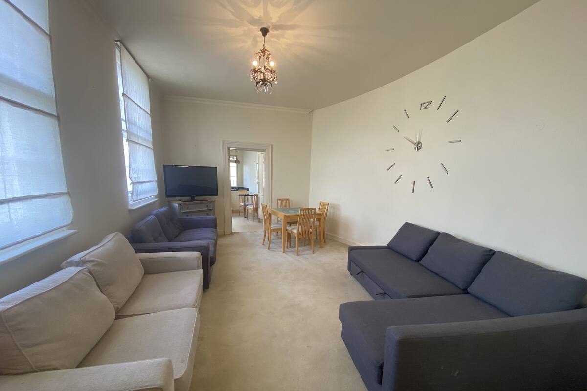 A living room with two sofas, a TV, a chandelier, and a wall clock.