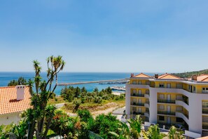 Hotel a la costa amb diversos balcons, vista al mar i un espigó rocoso al fons.