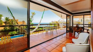Un balcón con vista al mar, una piscina y un área de comedor con sillas y una mesa.