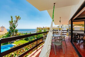 Un balcó amb vista al mar, una piscina i una zona de menjador amb cadires i taules.
