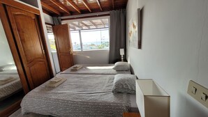Una habitación con dos camas, vigas de madera en el techo, un ventanal con vistas y una puerta.