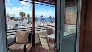 Un balcón con vista al mar, palmeras y sillas de playa.