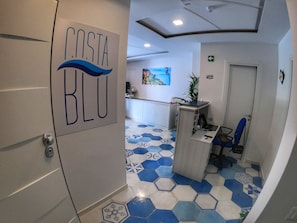 A reception area with a Costa Blu sign, a counter, a chair, and a wall-mounted TV. - Costa Blu (Agerola)