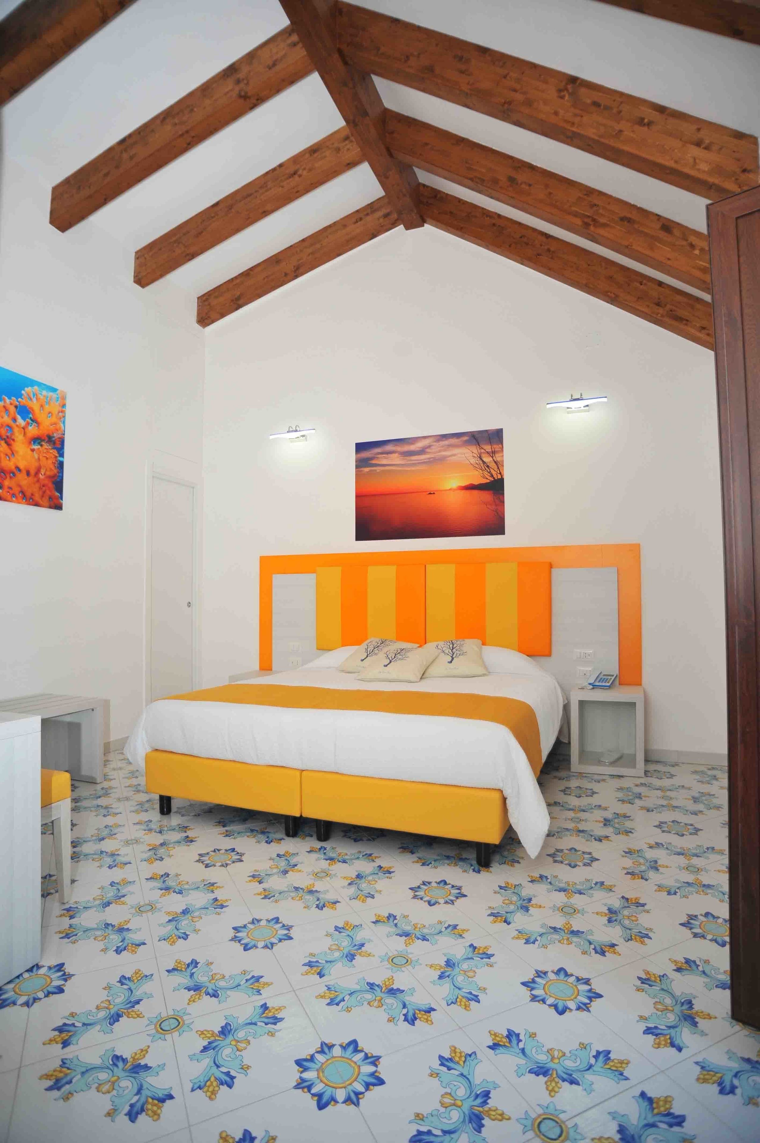 A bedroom with a bed, wooden beams, a painting, and patterned floor tiles.
