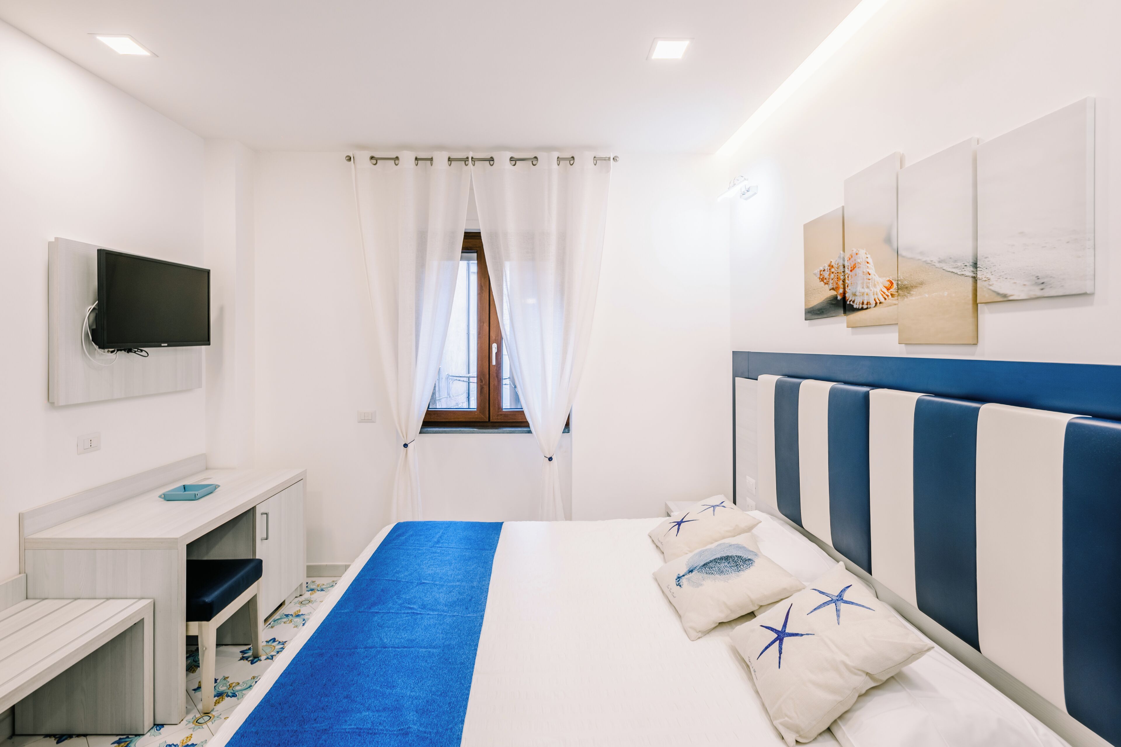 A hotel room with a bed, a desk, a television, and artwork on the walls.