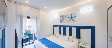 A hotel room with a bed, a bedside table with a phone, a window with curtains, and a view of the outside.