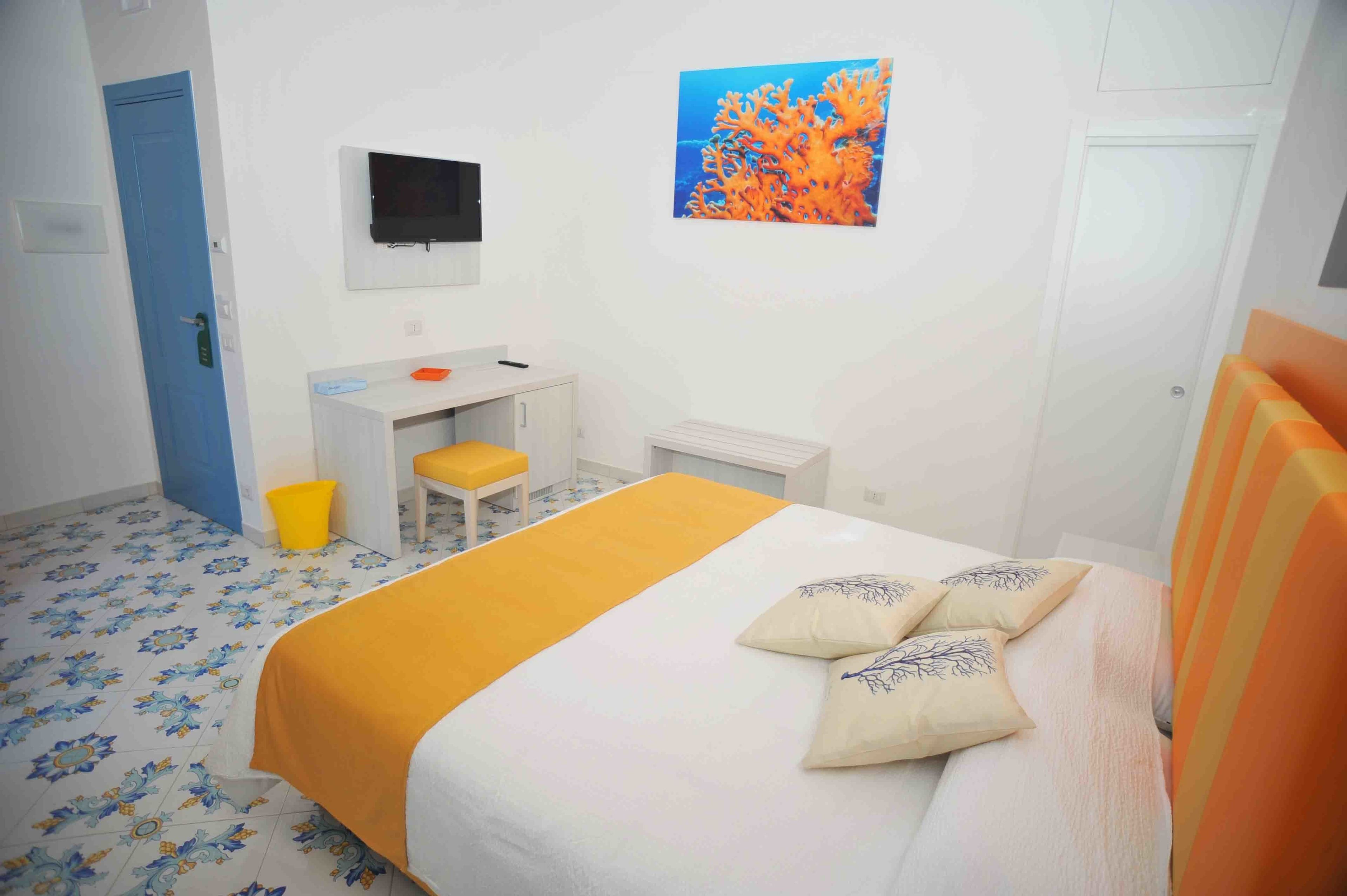 A hotel room with a bed, a desk, a chair, a television, and a painting on the wall.
