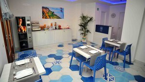 Un coin repas avec un sol carrelé à motifs hexagonaux, une table centrale entourée de chaises, un réfrigérateur, une plante et un tableau accroché au mur.