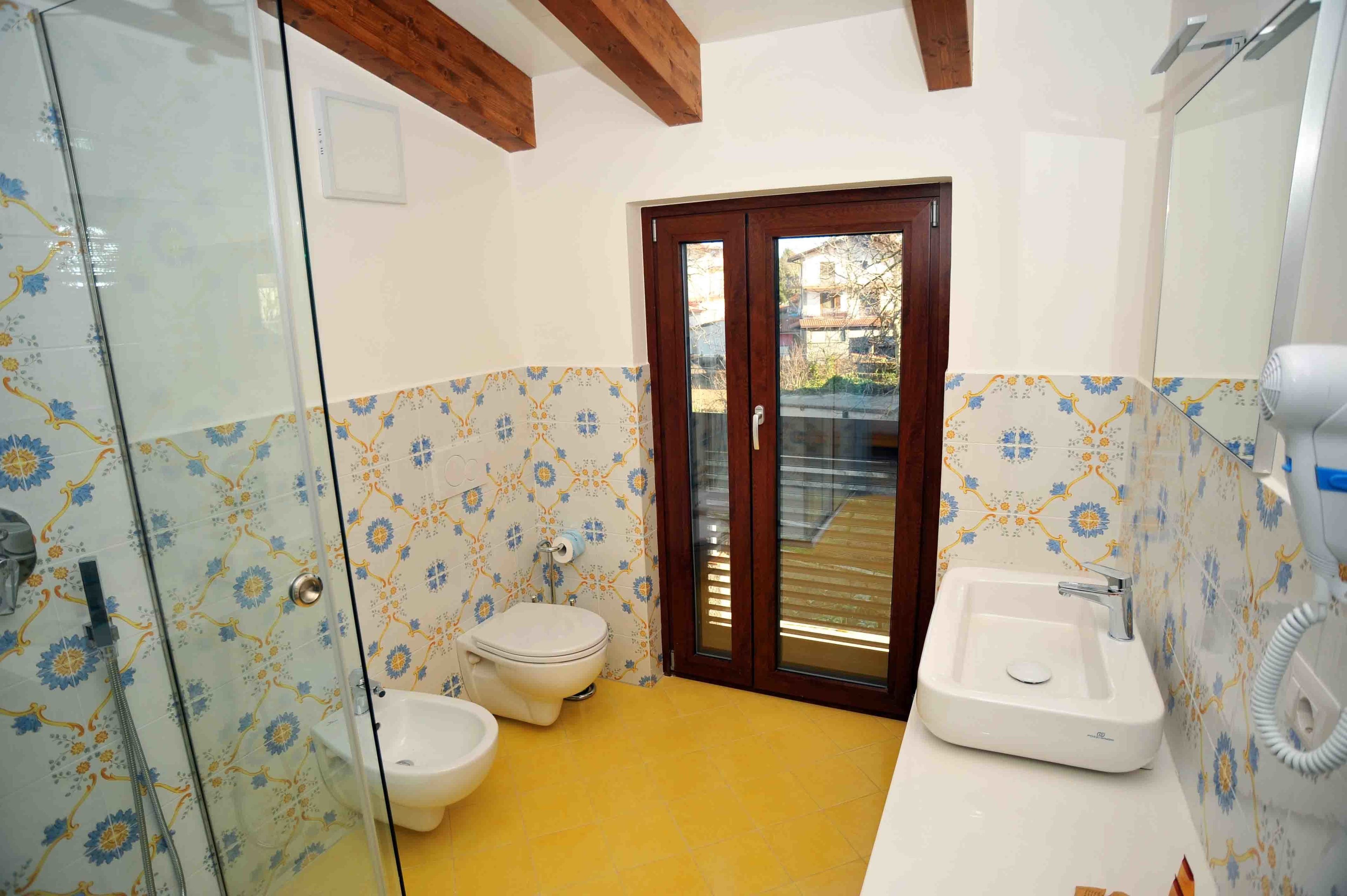Un baño con ducha, inodoro y lavamanos, con azulejos estampados y vigas de madera.